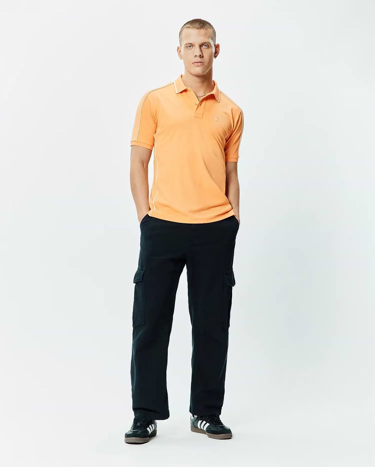 Mens Rhys Sport Polo, a classic fit peach pique polo with white piping on shoulders and collar, featuring a small embroidered Psycho Bunny skull logo on the left chest.