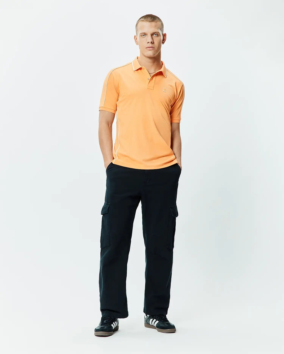 Mens Rhys Sport Polo, a classic fit peach pique polo with white piping on shoulders and collar, featuring a small embroidered Psycho Bunny skull logo on the left chest.