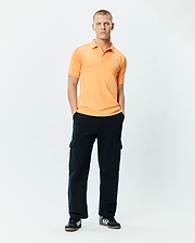Mens Rhys Sport Polo, a classic fit peach pique polo with white piping on shoulders and collar, featuring a small embroidered Psycho Bunny skull logo on the left chest.