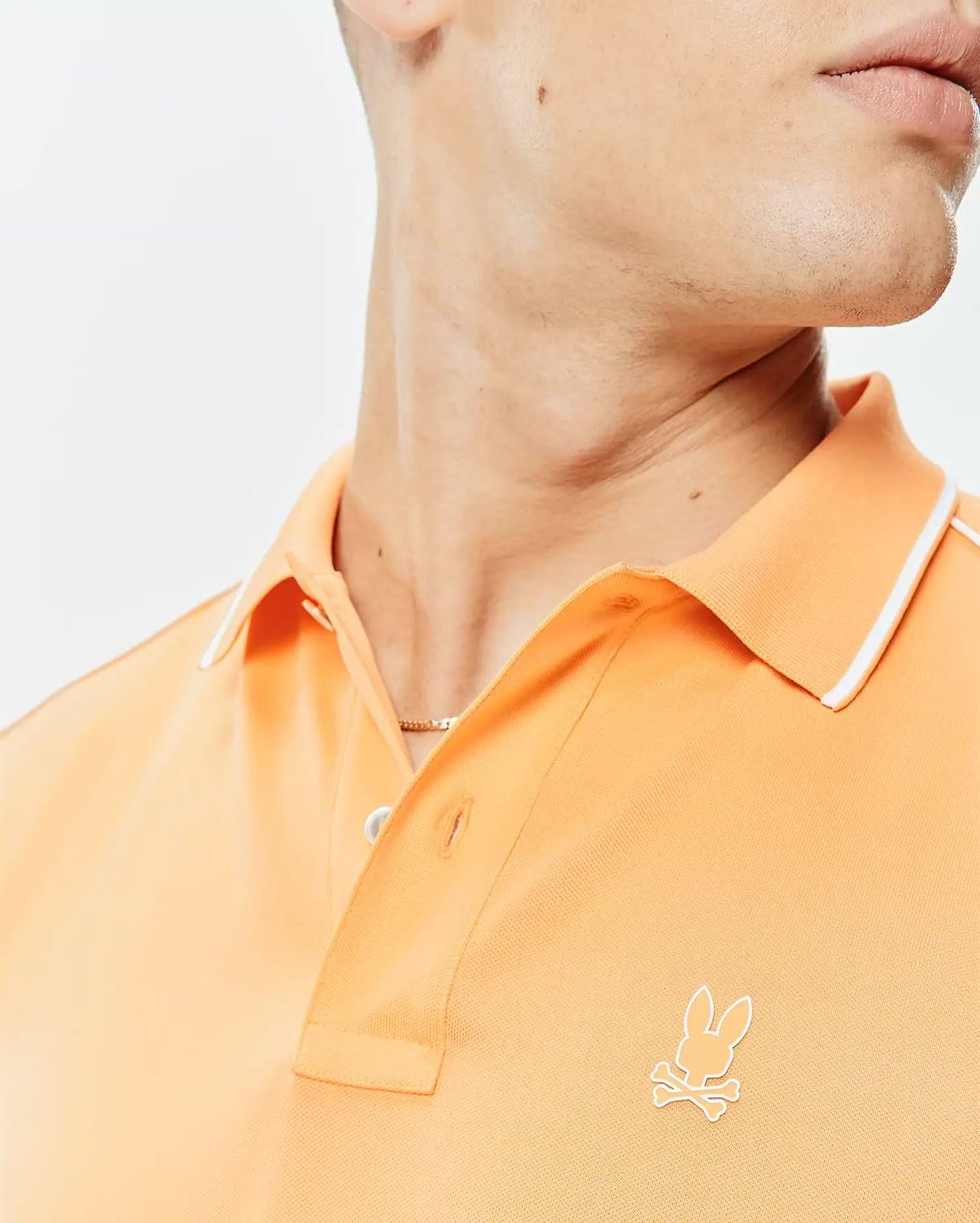 Mens Rhys Sport Polo in peach pique knit, featuring a classic fit, white tipped collar, two-button placket, and a small embroidered white Psycho Bunny skull logo on the left chest.