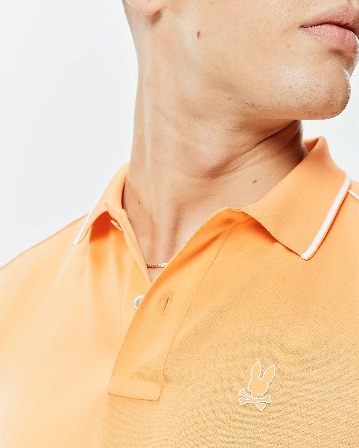 Mens Rhys Sport Polo in peach pique knit, featuring a classic fit, white tipped collar, two-button placket, and a small embroidered white Psycho Bunny skull logo on the left chest.