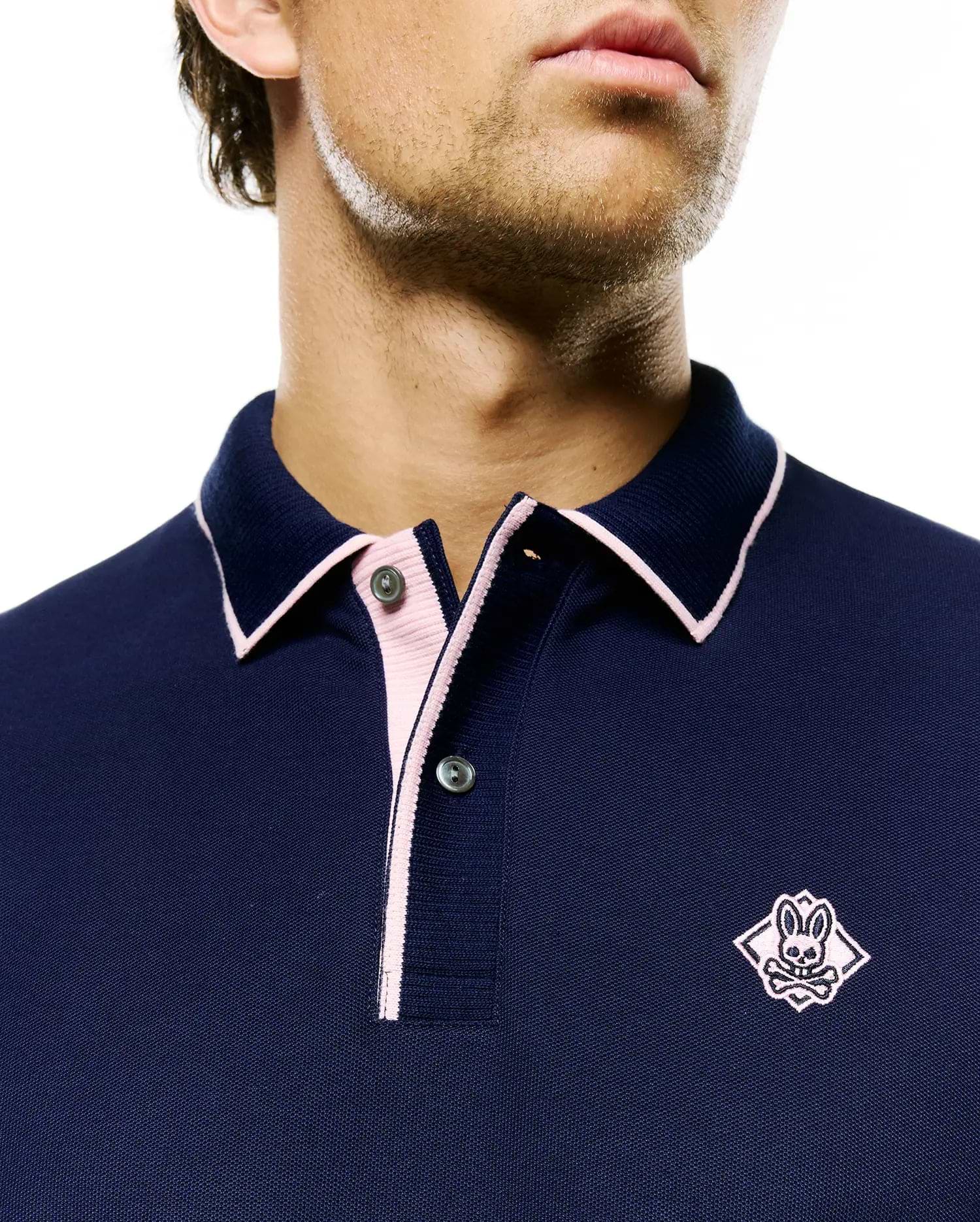 Mens Robin Pique Polo in navy pique knit, featuring a classic fit, pink contrast tipping on the collar and placket, and a pink embroidered Psycho Bunny skull logo on the left chest.