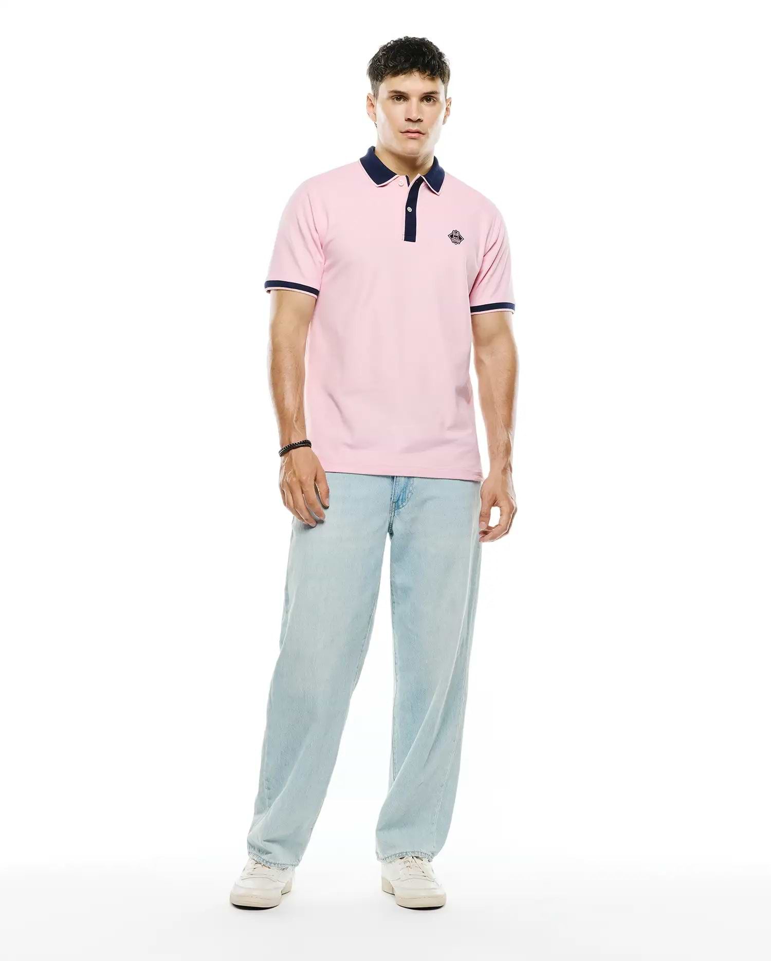 Mens Robin Pique Polo in classic fit pink pique fabric, featuring a navy blue collar, two-button placket, navy and white striped ribbed cuffs, and a small embroidered Psycho Bunny skull logo on the left chest.