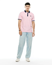 Mens Robin Pique Polo in classic fit pink pique fabric, featuring a navy blue collar, two-button placket, navy and white striped ribbed cuffs, and a small embroidered Psycho Bunny skull logo on the left chest.
