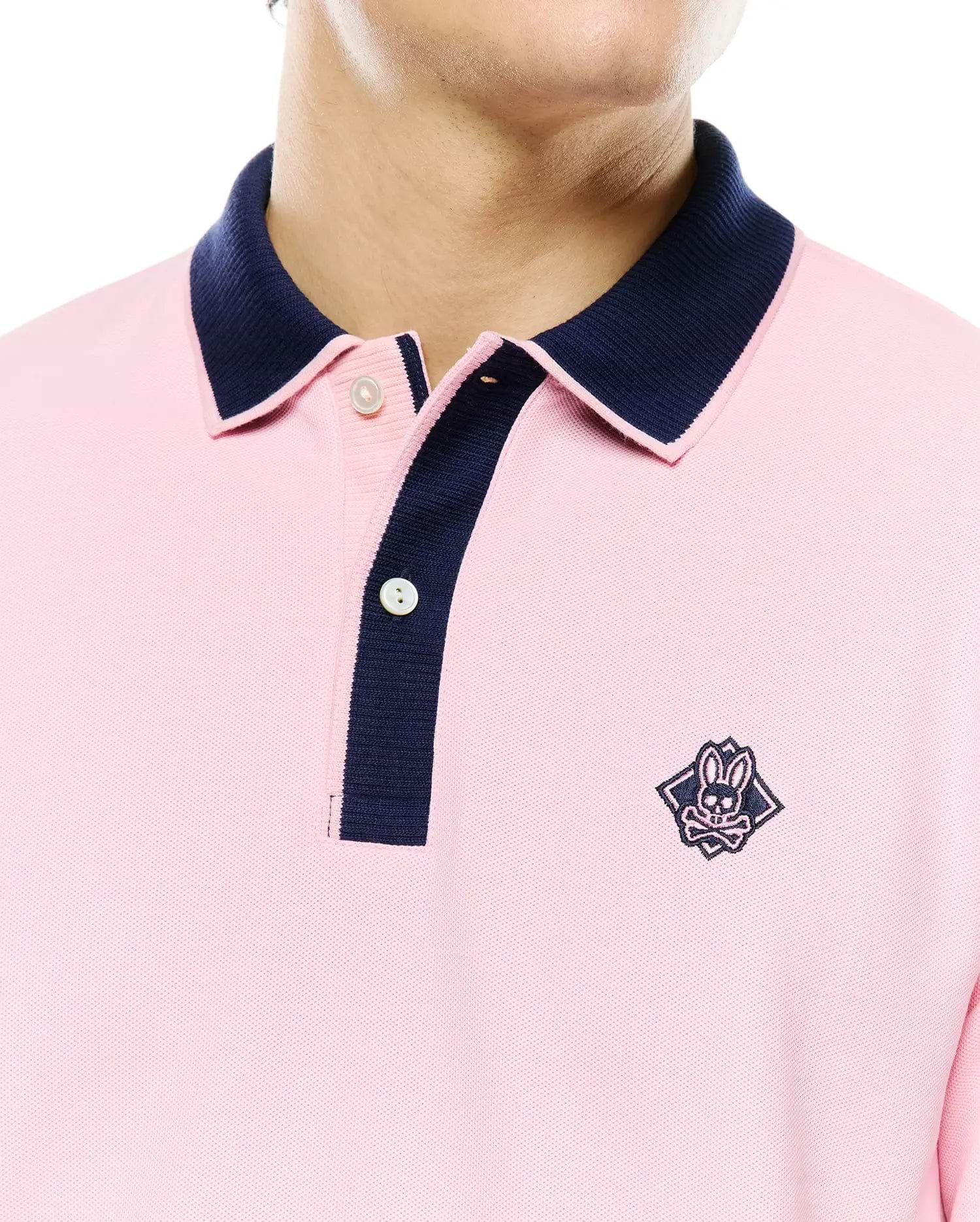 Mens Robin Pique Polo in pink pique fabric with a classic fit, featuring a navy blue contrast collar and placket, and an embroidered Psycho Bunny skull logo on the left chest.