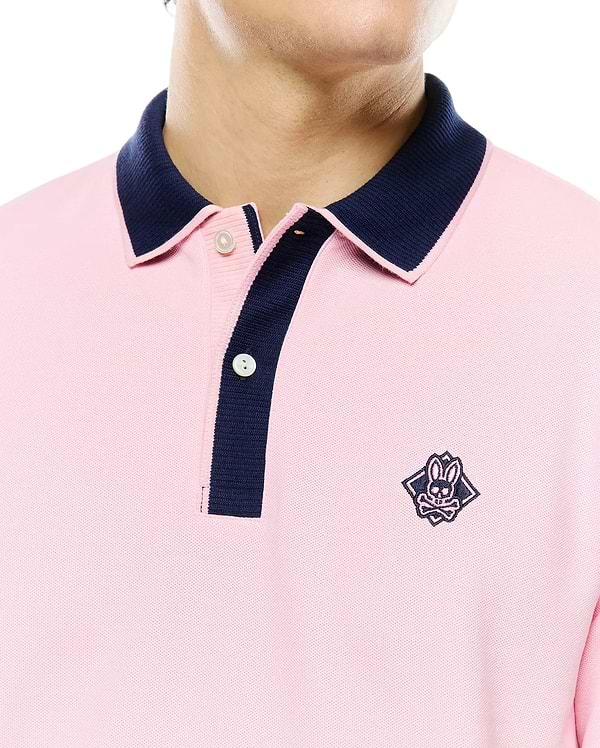 Mens Robin Pique Polo in pink pique fabric with a classic fit, featuring a navy blue contrast collar and placket, and an embroidered Psycho Bunny skull logo on the left chest.