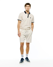 Mens Robin Pique Polo in cream with navy collar and cuff tipping, featuring a small embroidered Psycho Bunny skull logo on the left chest, paired with matching cream drawstring shorts.