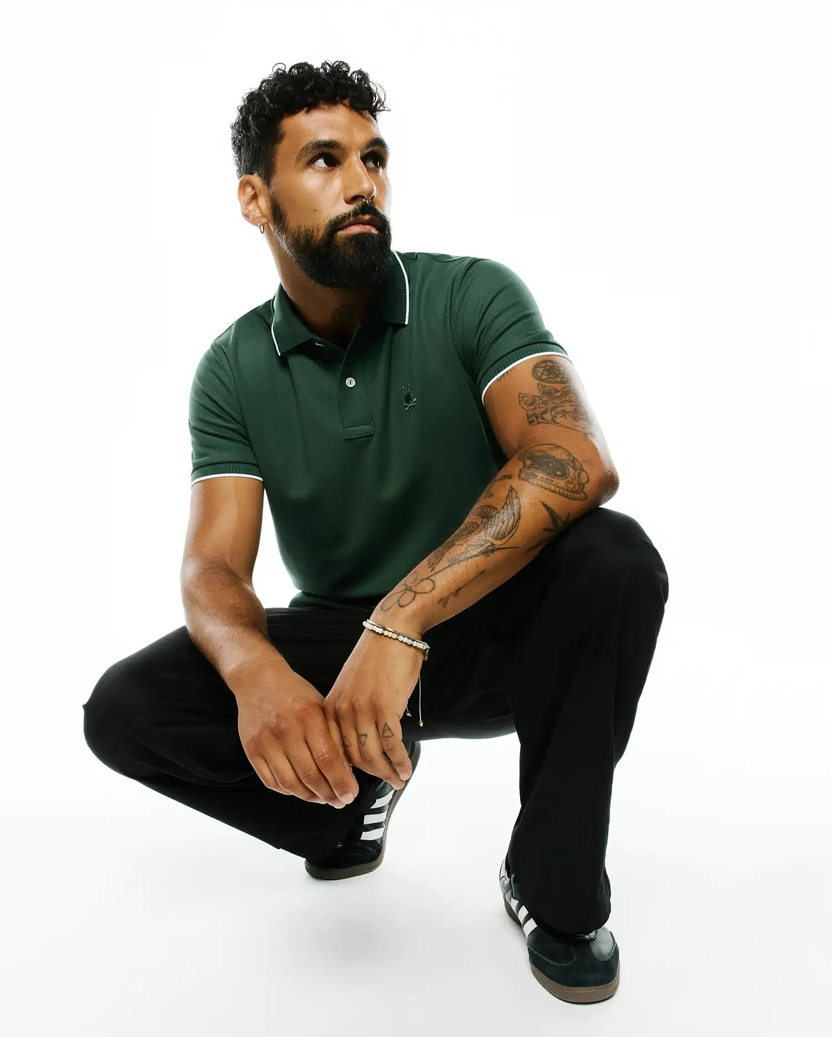 Mens Ringston Pique Polo in dark green, featuring a classic fit, pique knit fabric, white tipping on the collar and cuffs, and a small embroidered Psycho Bunny skull logo on the left chest.