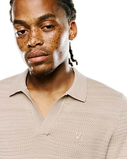 Mens Devon Braided Stitch Knit Polo in beige, featuring a unique braided stitch knit texture, spread collar, V-neck placket, and a small embroidered Psycho Bunny skull logo on the left chest.