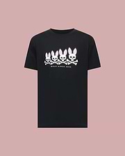 The Psycho Bunny MENS ARCHIVE GRADIANT BUNNY GRAPHIC TEE (MT0200029) is a black tee featuring four iconic Bunny skull and crossbones with pink ears above "BOLD SINCE 2005," set against a plain pink background.