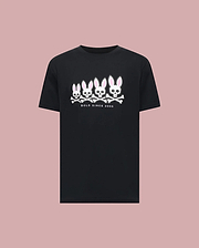 The Psycho Bunny MENS ARCHIVE GRADIANT BUNNY GRAPHIC TEE (MT0200029) is a black tee featuring four iconic Bunny skull and crossbones with pink ears above "BOLD SINCE 2005," set against a plain pink background.