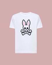 The Psycho Bunny MENS ARCHIVE BUNNY GRAPHIC TEE (MT0200031) is a white Pima cotton shirt with a bold front graphic of a skull with bunny ears and crossed bones, shown on a light pink background.