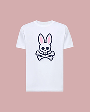 The Psycho Bunny MENS ARCHIVE BUNNY GRAPHIC TEE (MT0200031) is a white Pima cotton shirt with a bold front graphic of a skull with bunny ears and crossed bones, shown on a light pink background.