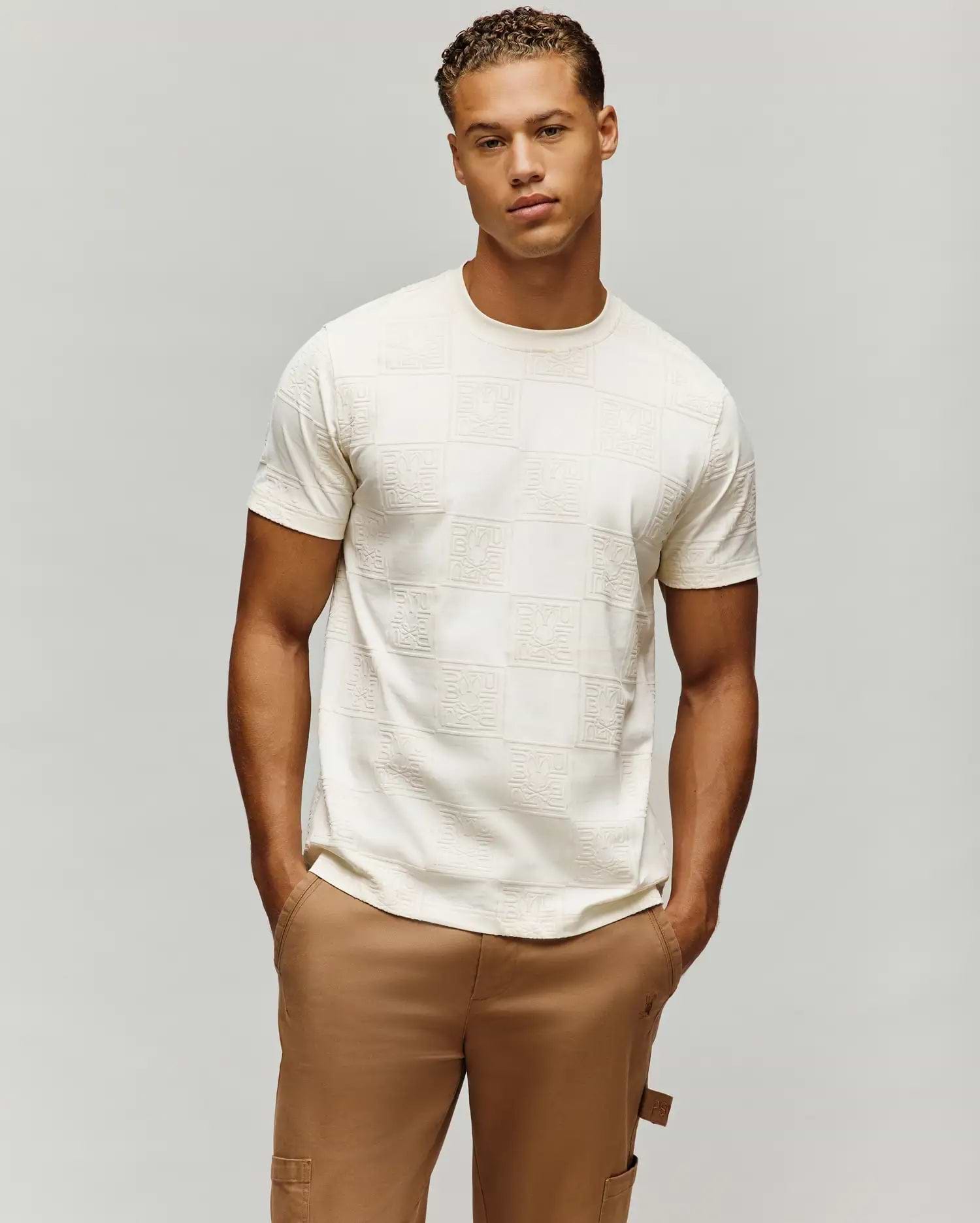 Mens Gio Tee, a cream classic fit jersey t-shirt featuring an all-over embossed checkerboard pattern with the iconic Psycho Bunny skull logo in each square.