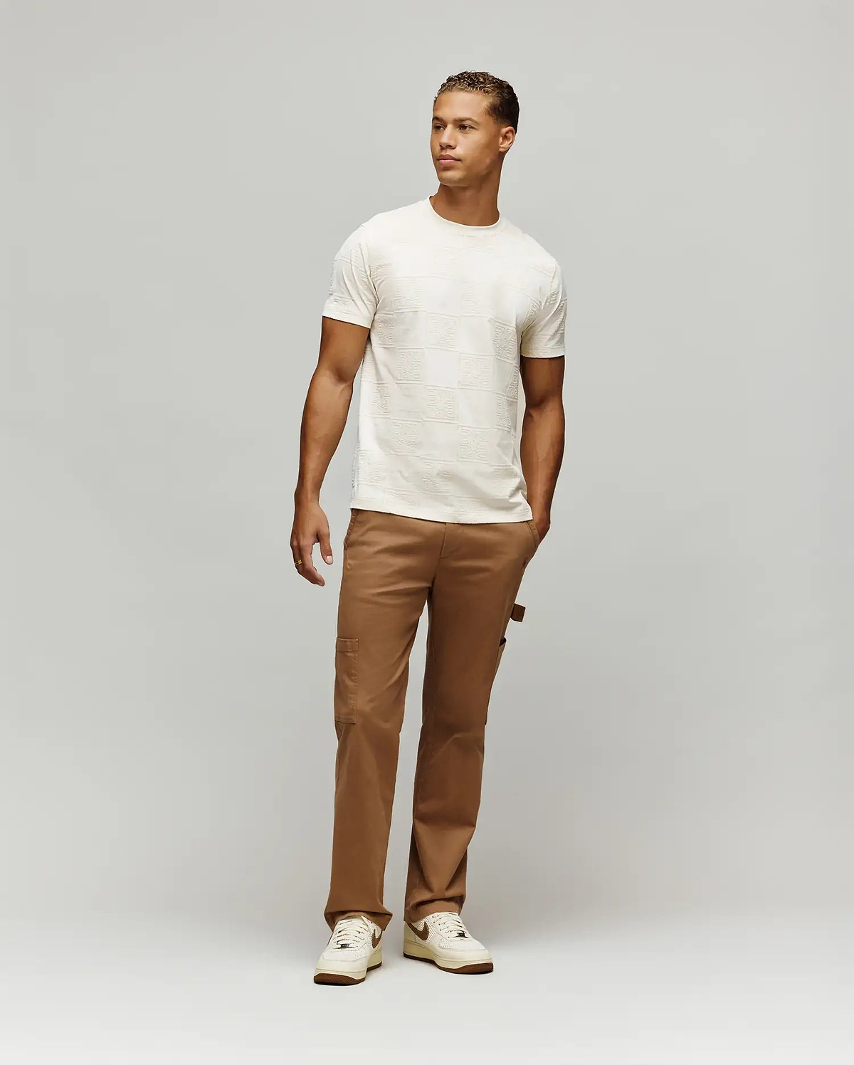 Mens Gio Tee cream textured jersey t-shirt with an all-over embossed checkerboard pattern featuring the iconic Psycho Bunny skull logo, designed for a comfortable classic fit.
