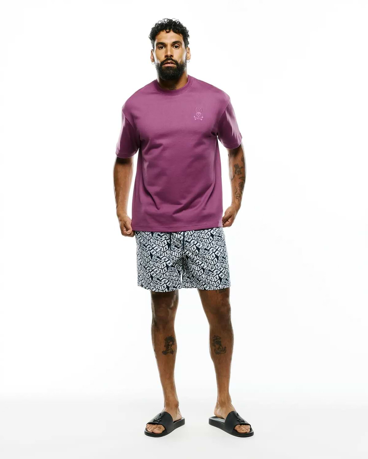 Mens Oscar Relaxed Fit Tee in plum jersey with a small embroidered Psycho Bunny skull logo on the left chest, paired with navy and white geometric pattern shorts.