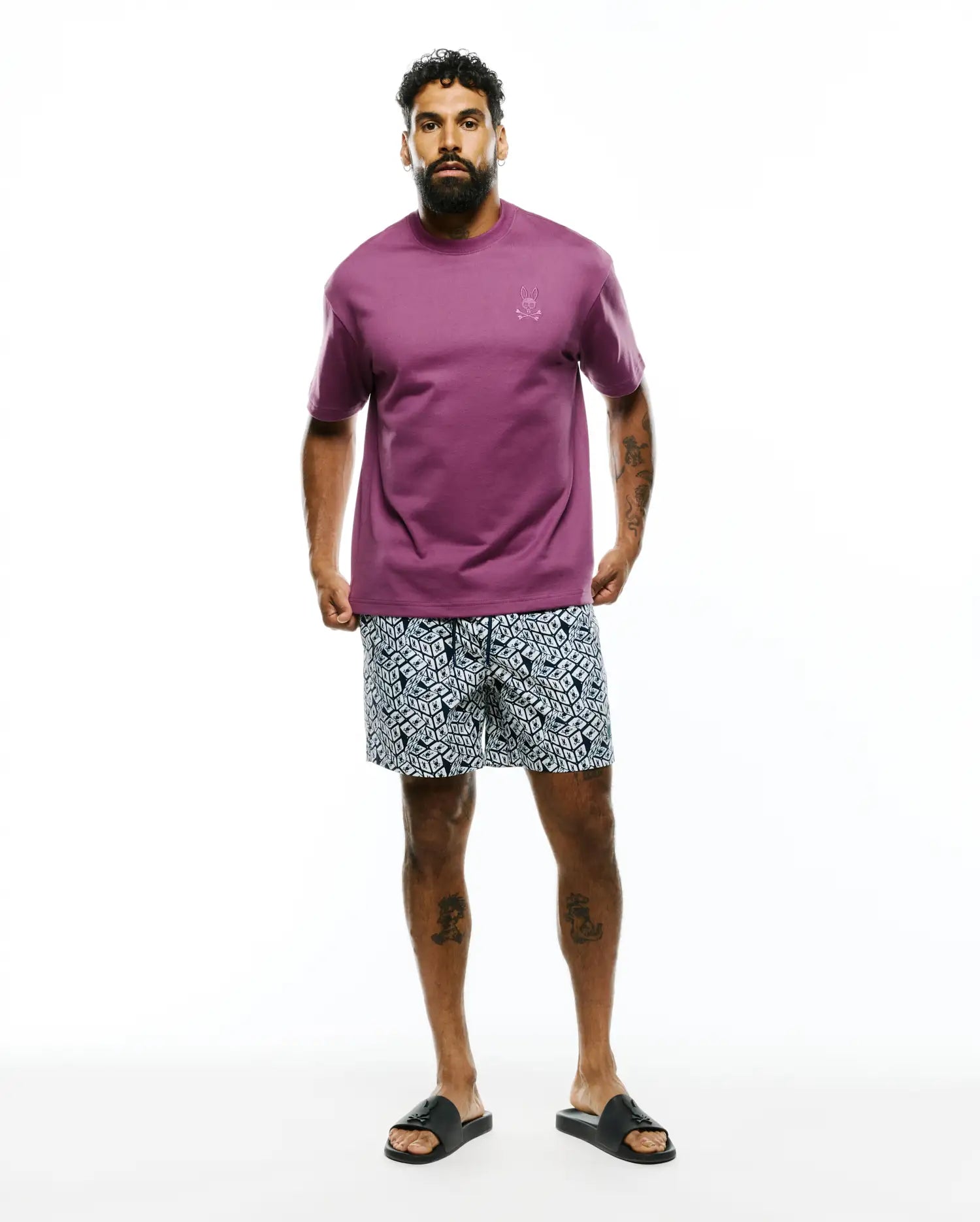 Mens Oscar Relaxed Fit Tee in plum jersey with a small embroidered Psycho Bunny skull logo on the left chest, paired with navy and white geometric pattern shorts.