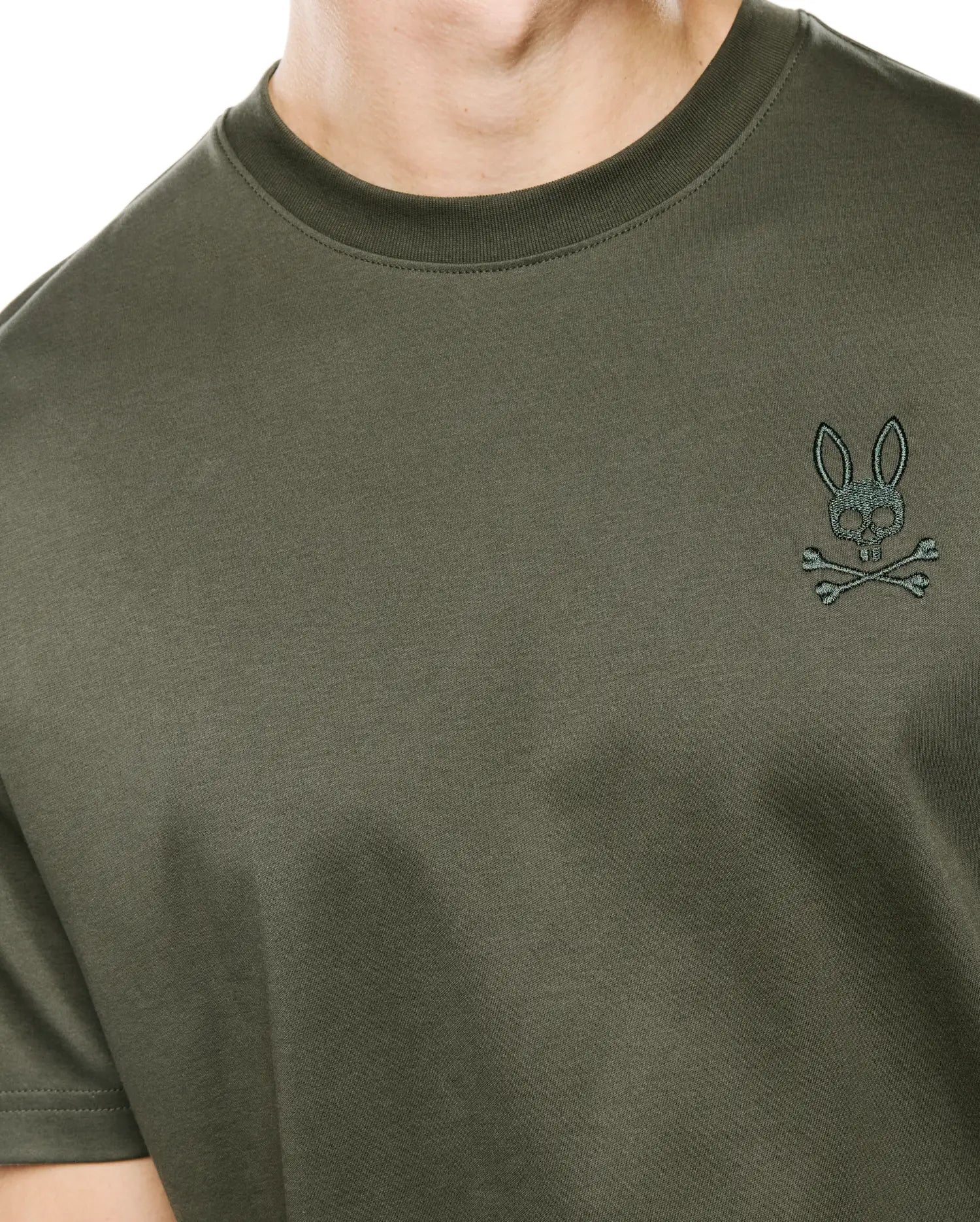 Mens Oscar Relaxed Fit Tee in deep olive green, crafted from soft jersey knit, featuring a small, intricately embroidered teal Psycho Bunny skull and crossbones logo on the left chest.