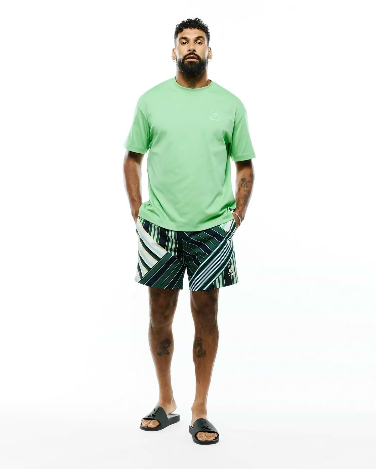 Mens Oscar Relaxed Fit Tee in light green jersey with a tonal embroidered bunny skull on the left chest, paired with dark green striped shorts featuring white, light green, and yellow accents and a small embroidered bunny skull on the leg.