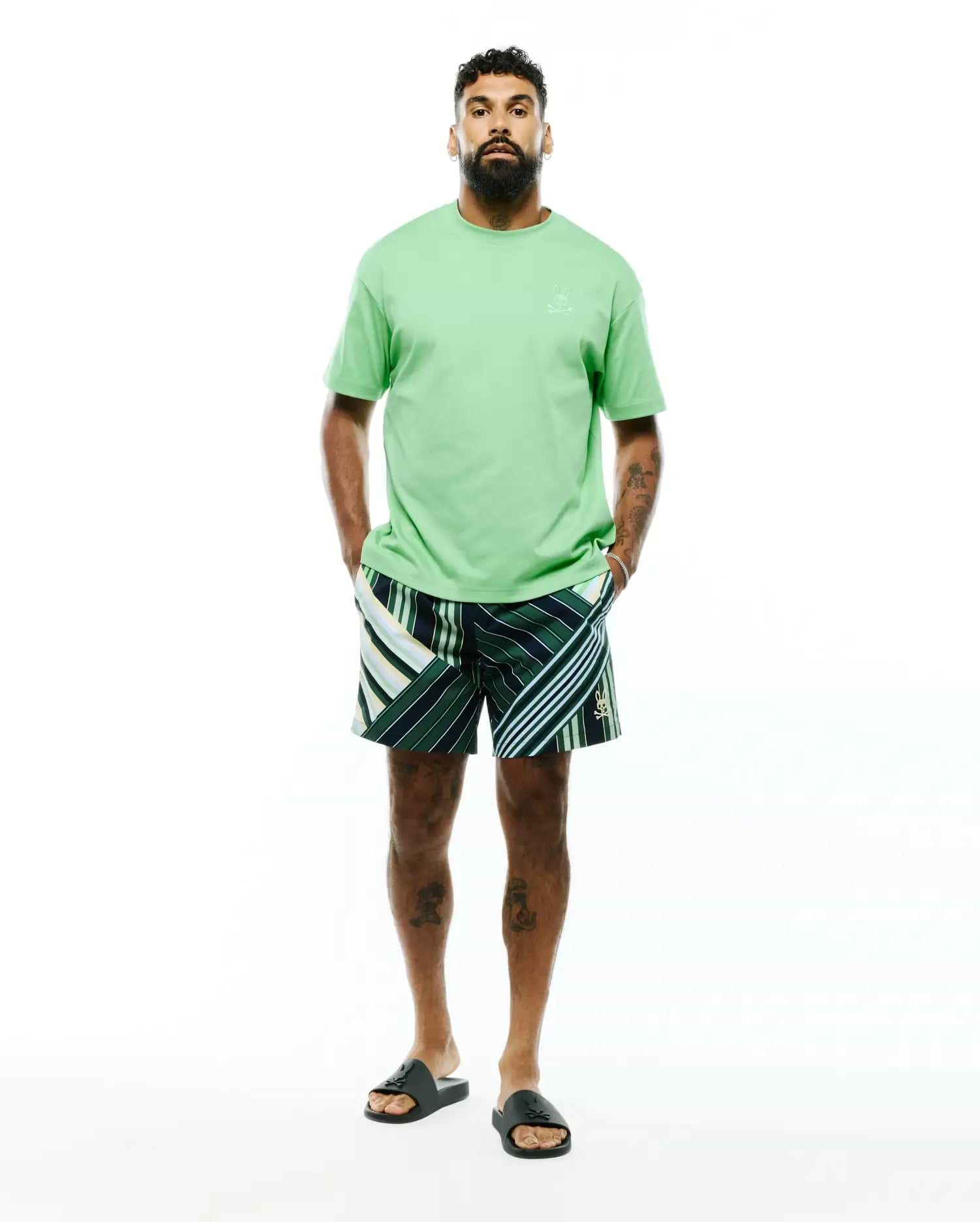 Mens Oscar Relaxed Fit Tee in light green jersey with a tonal embroidered bunny skull on the left chest, paired with dark green striped shorts featuring white, light green, and yellow accents and a small embroidered bunny skull on the leg.