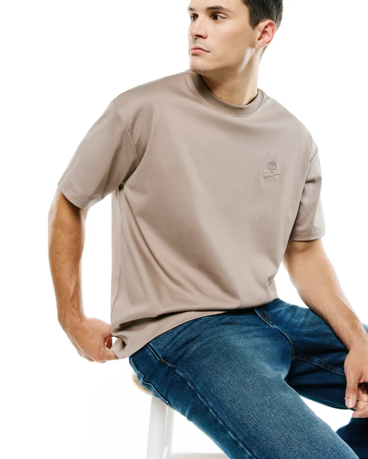 Men's Oscar Oversized Tee, a premium taupe jersey t-shirt with a relaxed fit, featuring a small, light grey embroidered Psycho Bunny skull logo on the left chest. (3)