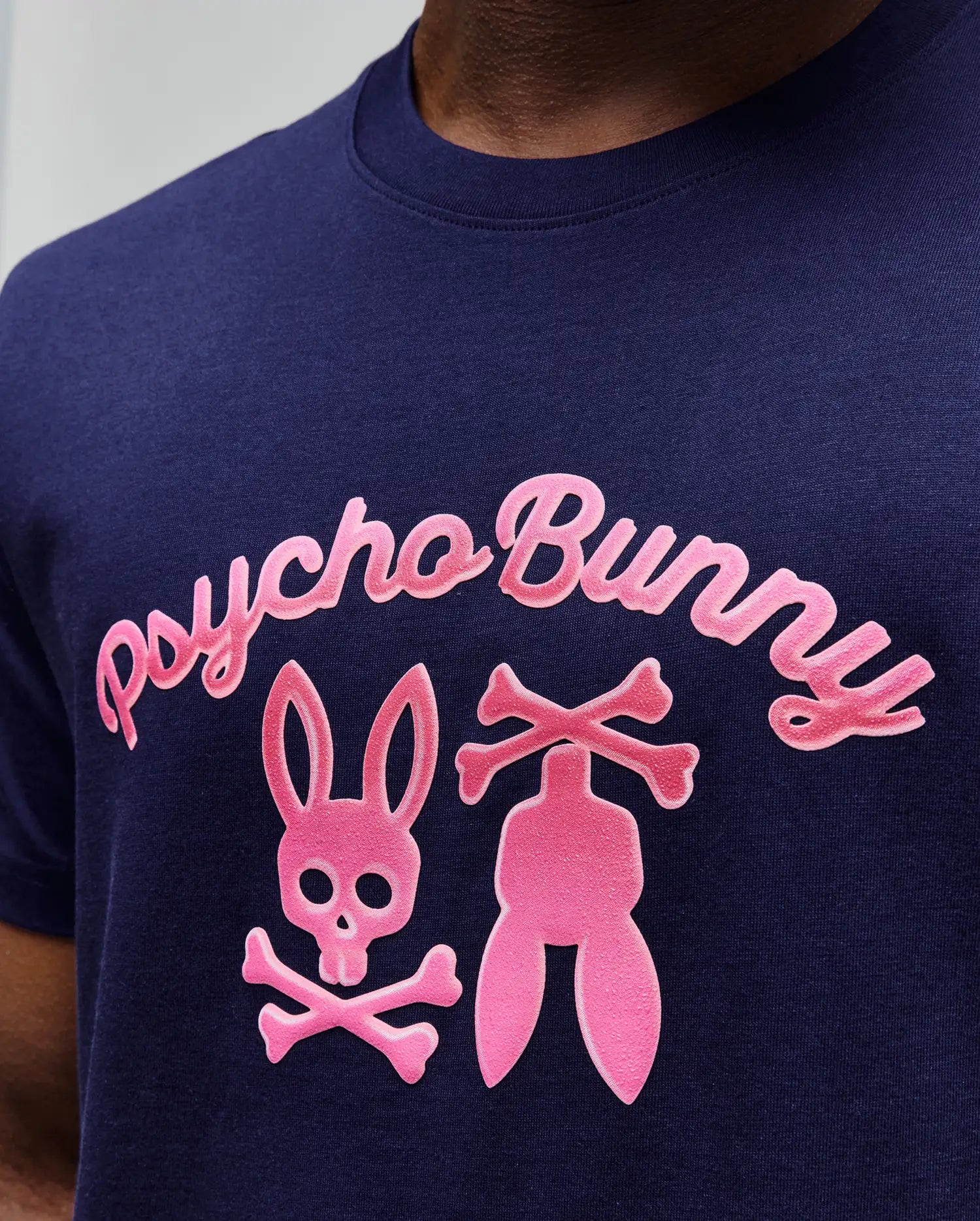 Mens Aram Graphic Tee in navy blue jersey, featuring a large, textured bright pink chest graphic with Psycho Bunny script, the iconic bunny skull, and crossed bones design for a classic fit.