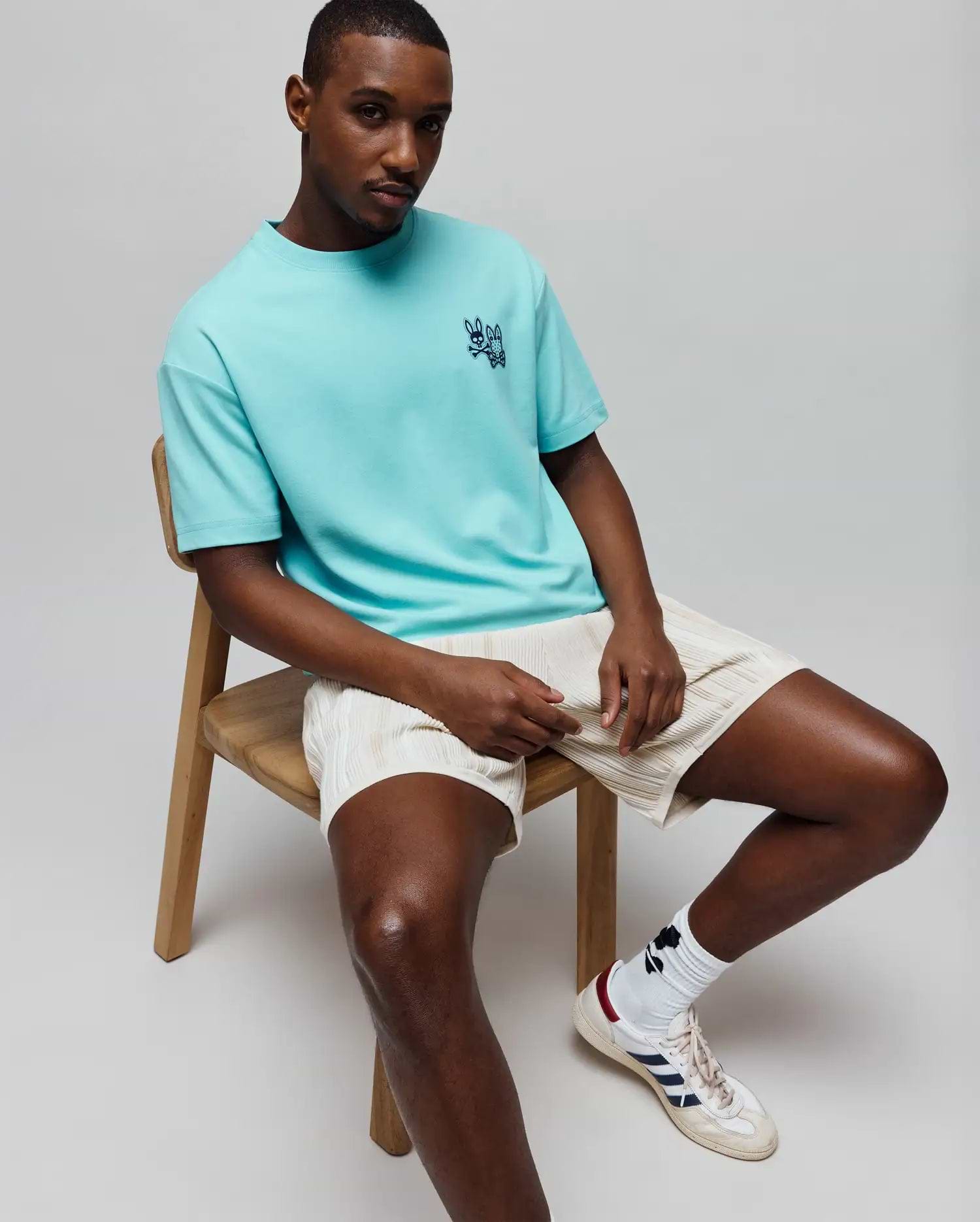 Mens Luke Back Graphic Tee, a relaxed fit aqua jersey t-shirt featuring a small, embroidered dark blue Psycho Bunny skull logo on the left chest.