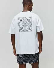 White Mens Luke Back Graphic Tee, relaxed jersey tee with a large black bandana graphic and four Psycho Bunny skull logos on the back, paired with black relaxed shorts with all-over white bandana-bunny skull pattern.