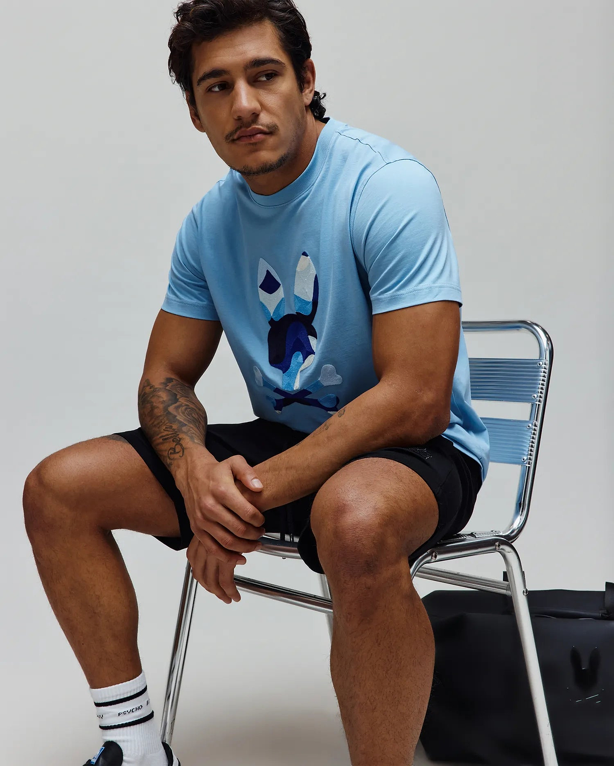 Mens Ara Graphic Tee, a light blue classic fit jersey knit t-shirt featuring a large, central graphic of the iconic Psycho Bunny skull logo in shades of blue, white, and black.