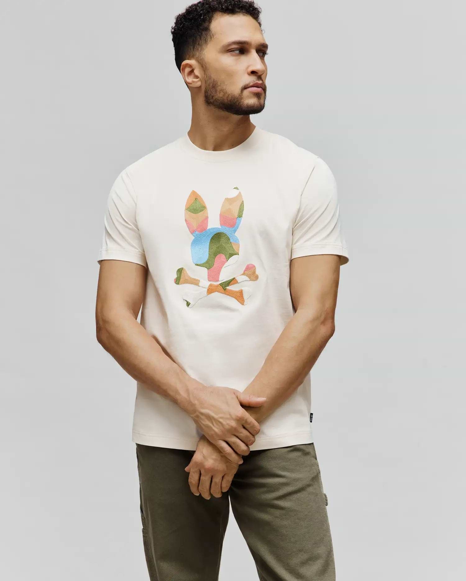 Cream Mens Ara Graphic Tee, classic fit jersey t-shirt featuring a large, geometric multi-color Psycho Bunny skull and crossbones graphic on the chest, with a small brand tag on the hem.