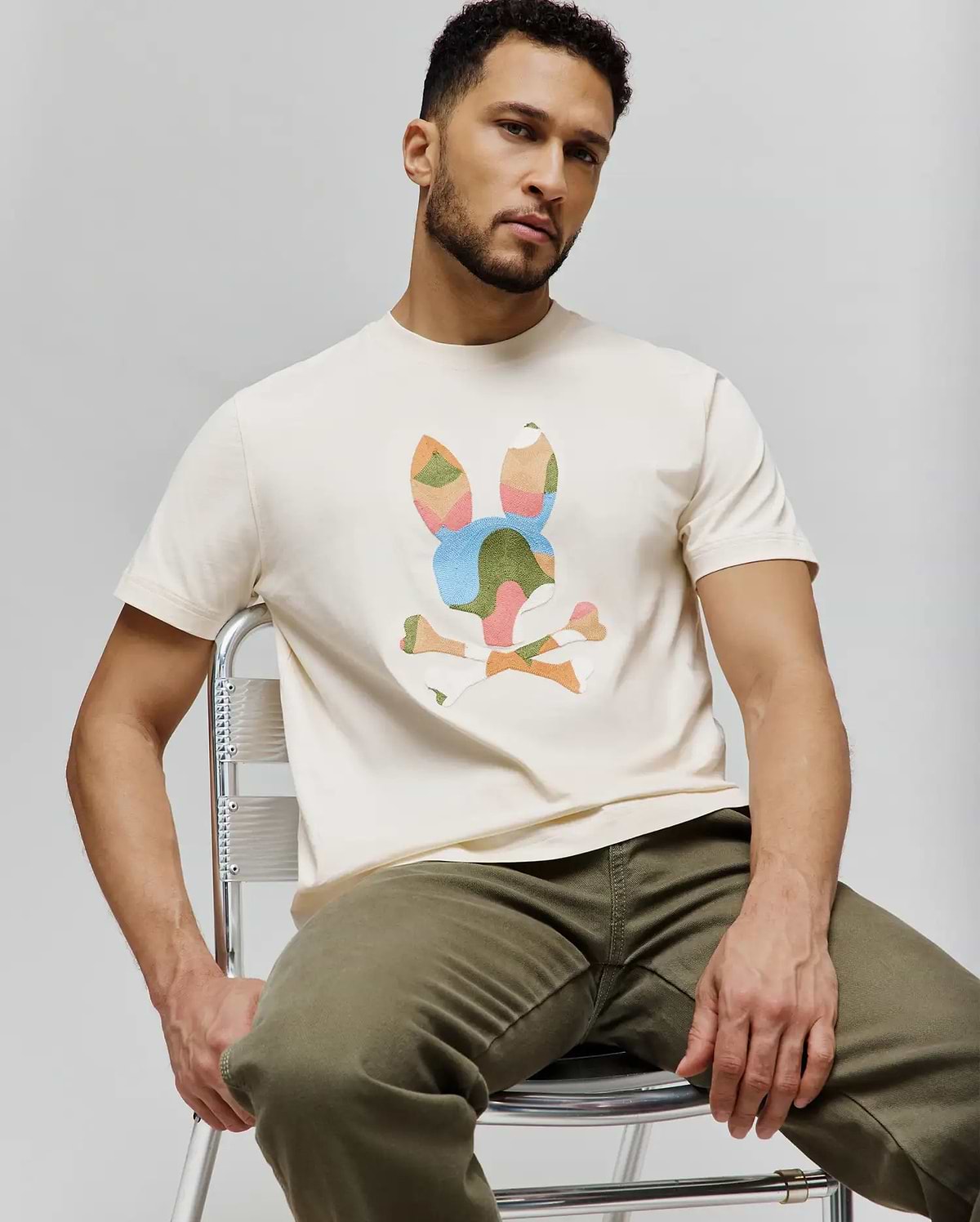 Mens Ara Graphic Tee, a classic fit cream jersey t-shirt featuring a large, multi-colored abstract Psycho Bunny skull logo graphic on the chest.