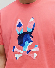 MENS ARA GRAPHIC TEE in coral jersey knit, featuring a large, central embroidered Psycho Bunny skull logo with geometric blue, pink, and white accents.