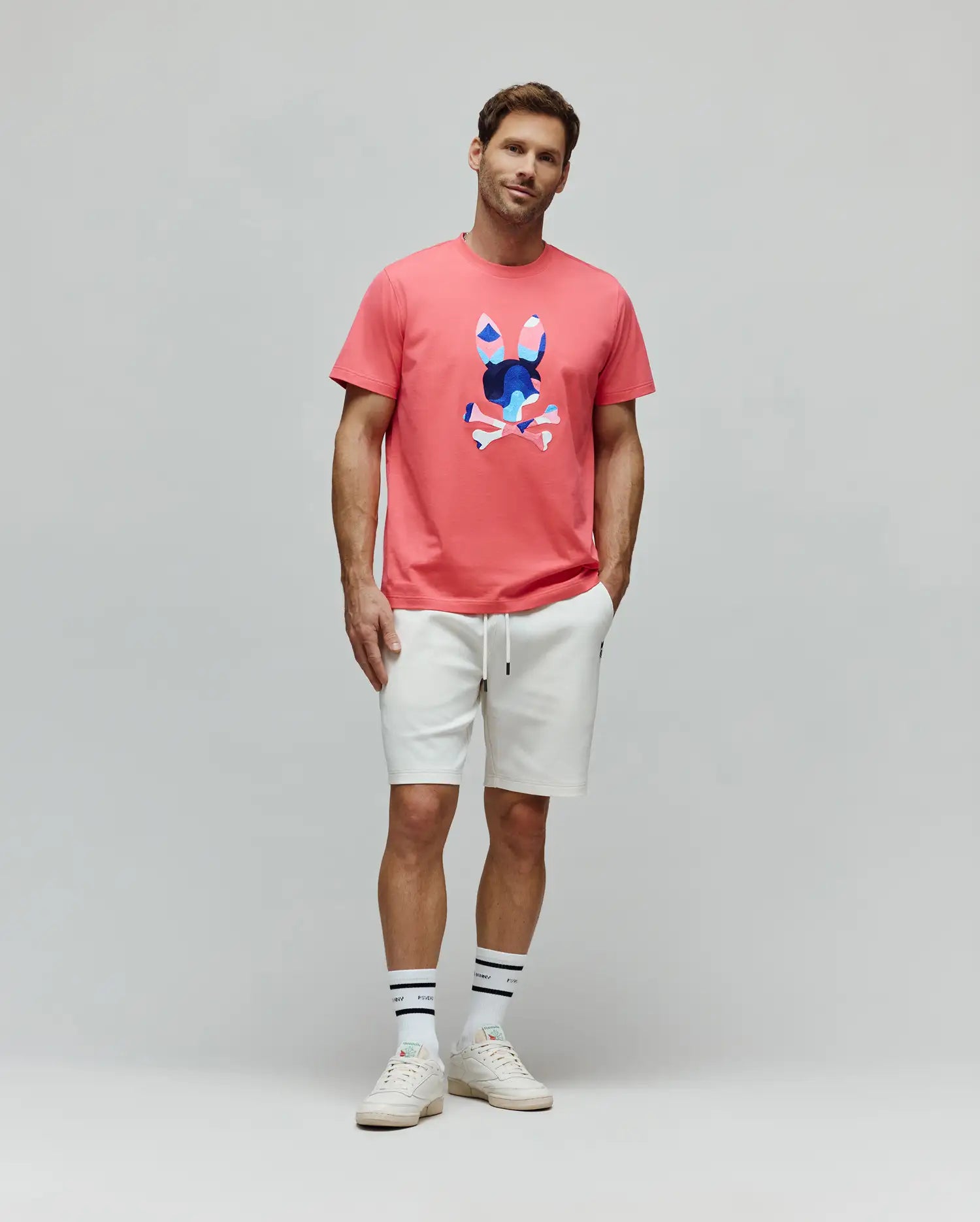 Mens Ara Graphic Tee in coral, featuring a classic fit jersey knit with a large, vibrant abstract blue and pink Psycho Bunny skull graphic on the center chest.