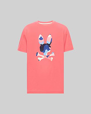 Mens Ara Graphic Tee in coral pink jersey, featuring a large central Psycho Bunny skull and crossbones logo with a vibrant blue, pink, and white abstract camouflage pattern, classic fit.