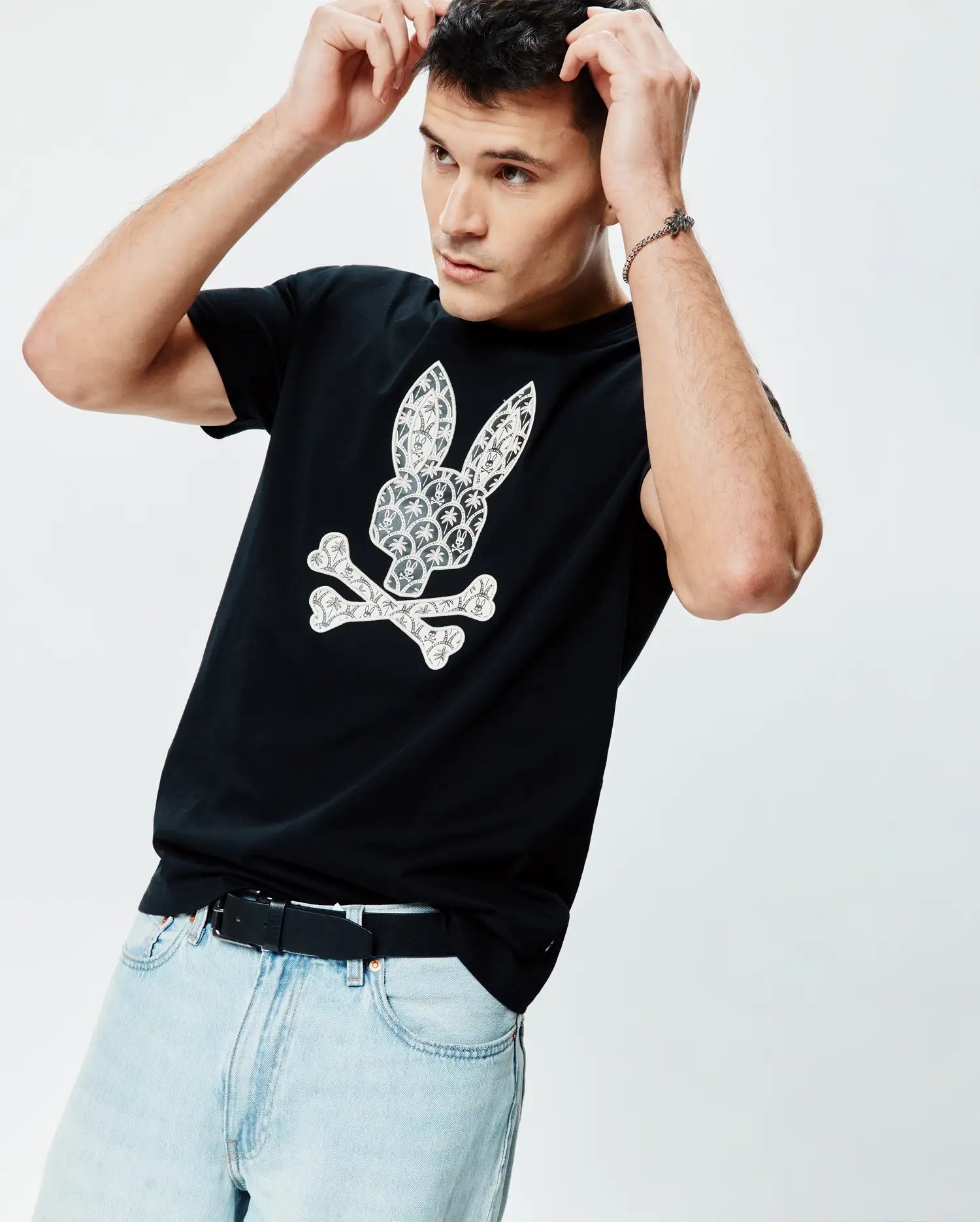 Mens Brad Graphic Tee, black cotton jersey, classic fit, featuring a large white Psycho Bunny skull and crossbones graphic on the chest with a detailed palm tree and mini bunny skull pattern.