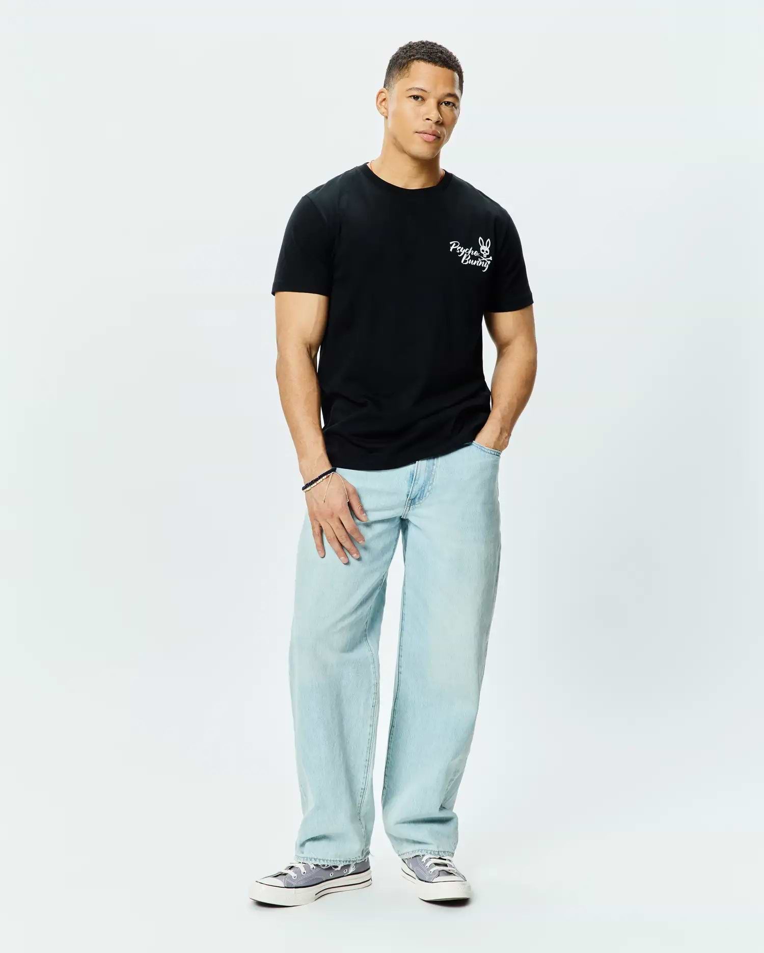 Mens Colin Back Graphic Tee, a black classic fit jersey t-shirt, features a small white embroidered Psycho Bunny skull logo and text on the left chest.