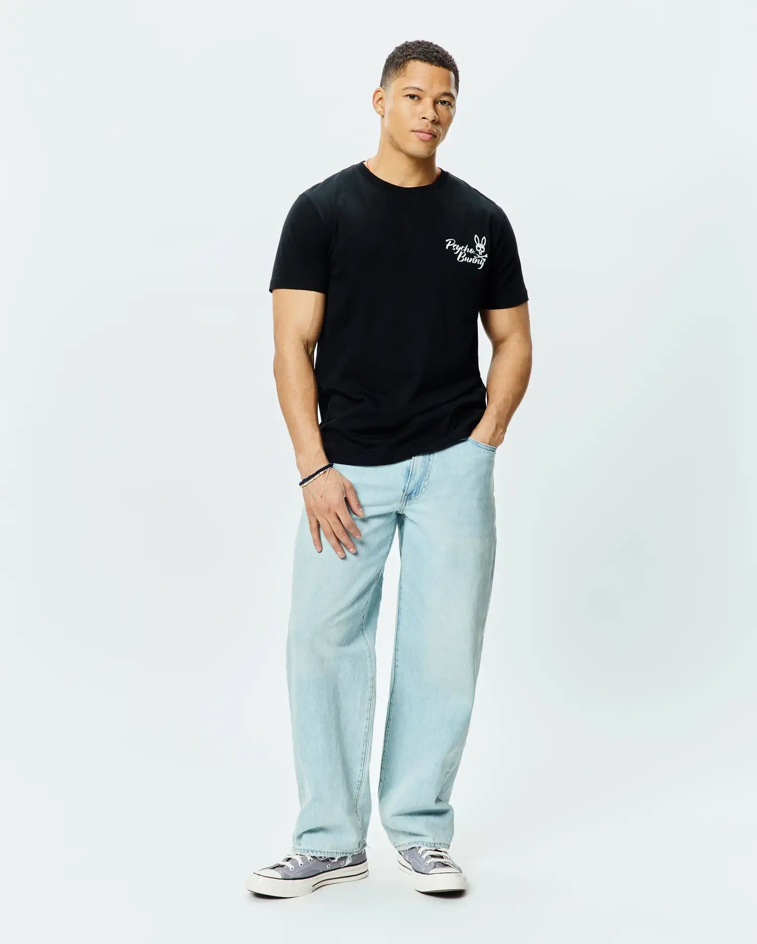 Mens Colin Back Graphic Tee, a black classic fit jersey t-shirt, features a small white embroidered Psycho Bunny skull logo and text on the left chest.