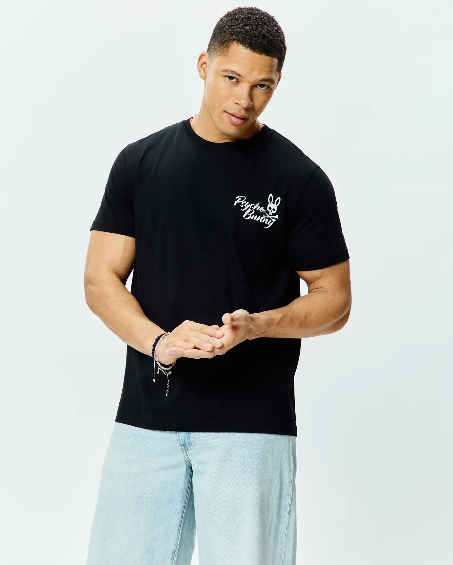 Mens Colin Back Graphic Tee, a black classic fit jersey t-shirt with a prominent white embroidered Psycho Bunny skull and crossbones logo and script text on the left chest.