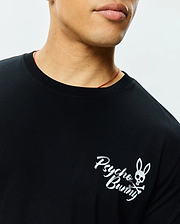 Black Mens Colin Back Graphic Tee, classic fit, smooth jersey knit, featuring a small white printed Psycho Bunny skull and crossbones logo with script on the left chest.