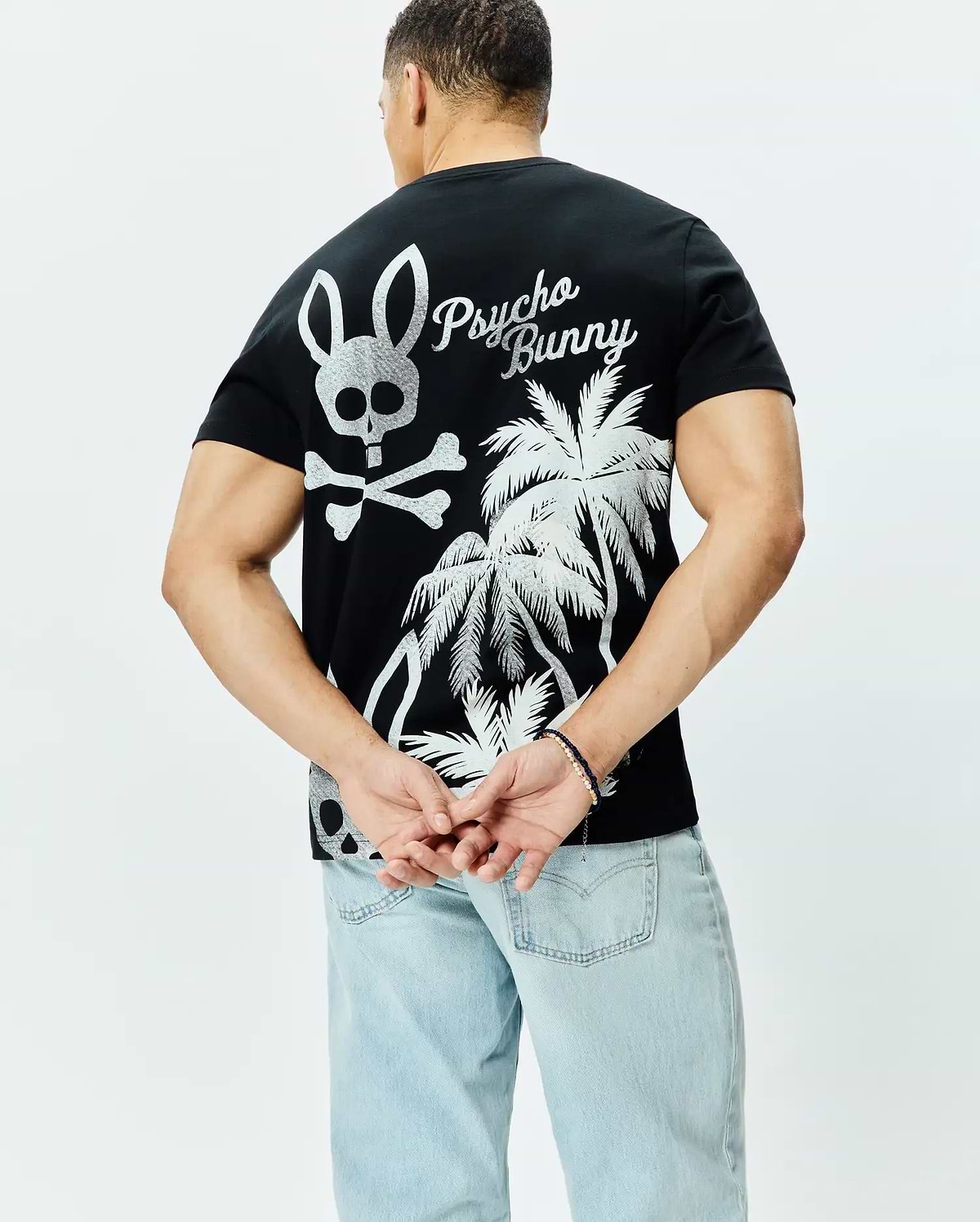 Mens Colin Back Graphic Tee, black jersey knit, classic fit, featuring a large silver Psycho Bunny skull and crossbones, script logo, and palm tree graphic on the back.