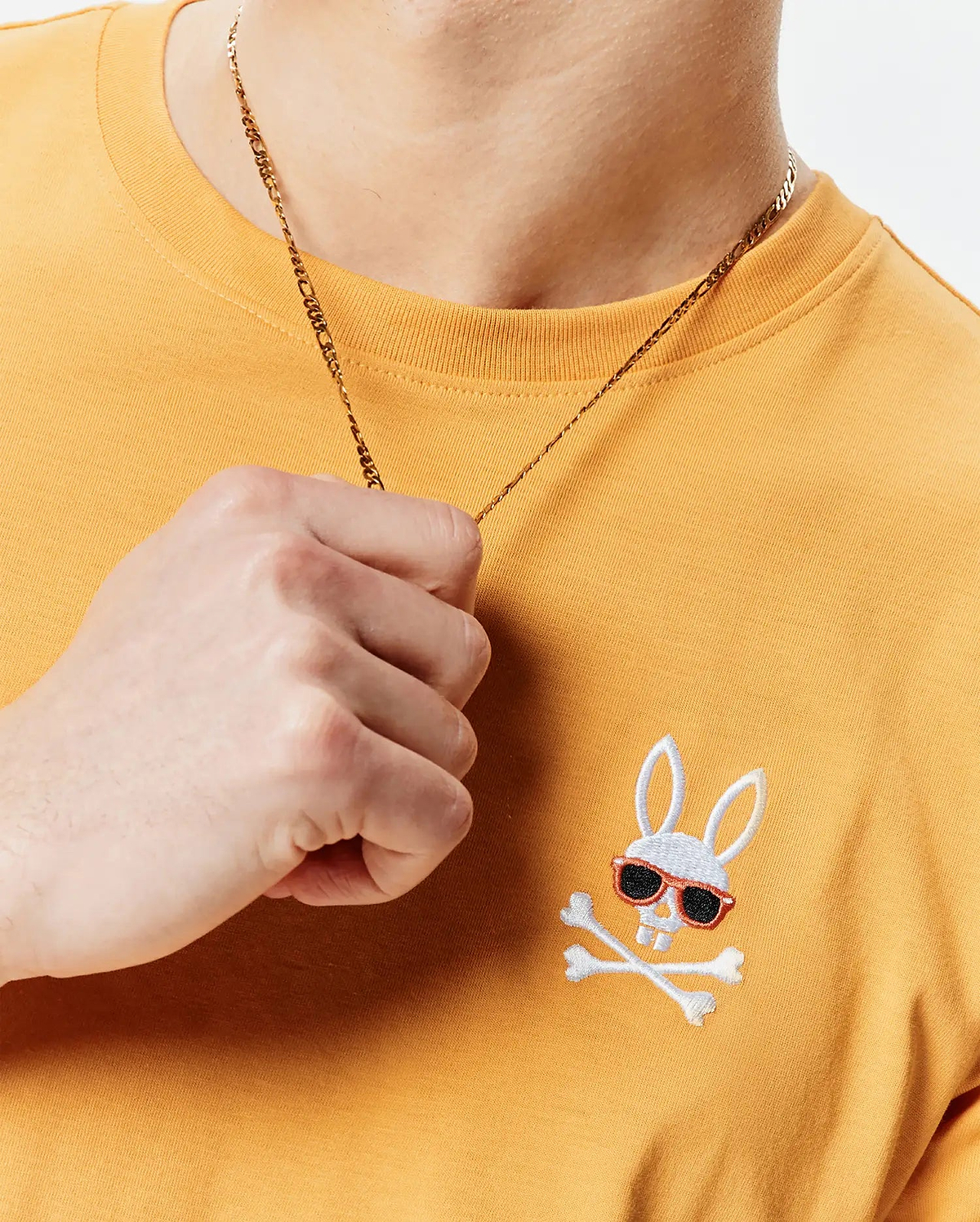 Mens Sunny Chest Graphic Tee, a classic fit mustard yellow jersey knit t-shirt with an embroidered white Psycho Bunny skull logo featuring red-framed black sunglasses and crossbones on the left chest.