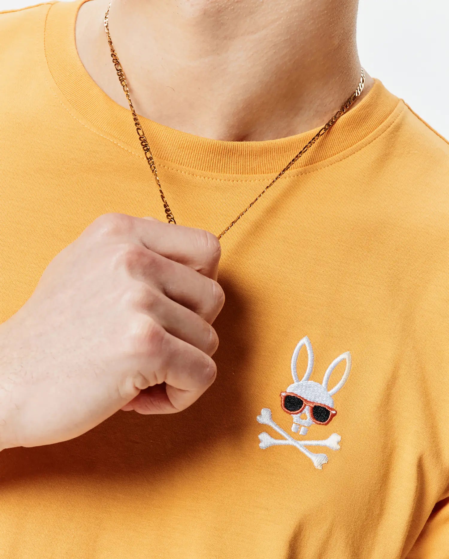 Mens Sunny Chest Graphic Tee, a classic fit mustard yellow jersey knit t-shirt with an embroidered white Psycho Bunny skull logo featuring red-framed black sunglasses and crossbones on the left chest.