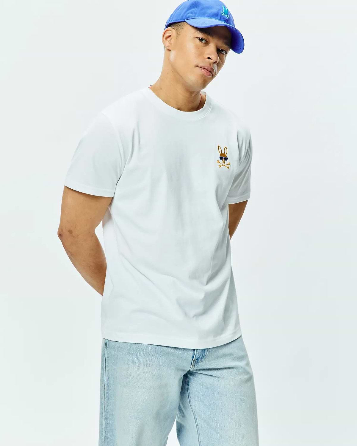 Mens Sunny Chest Graphic Tee, a classic fit white jersey t-shirt featuring a small embroidered brown Psycho Bunny skull logo with blue sunglasses and crossbones on the left chest.