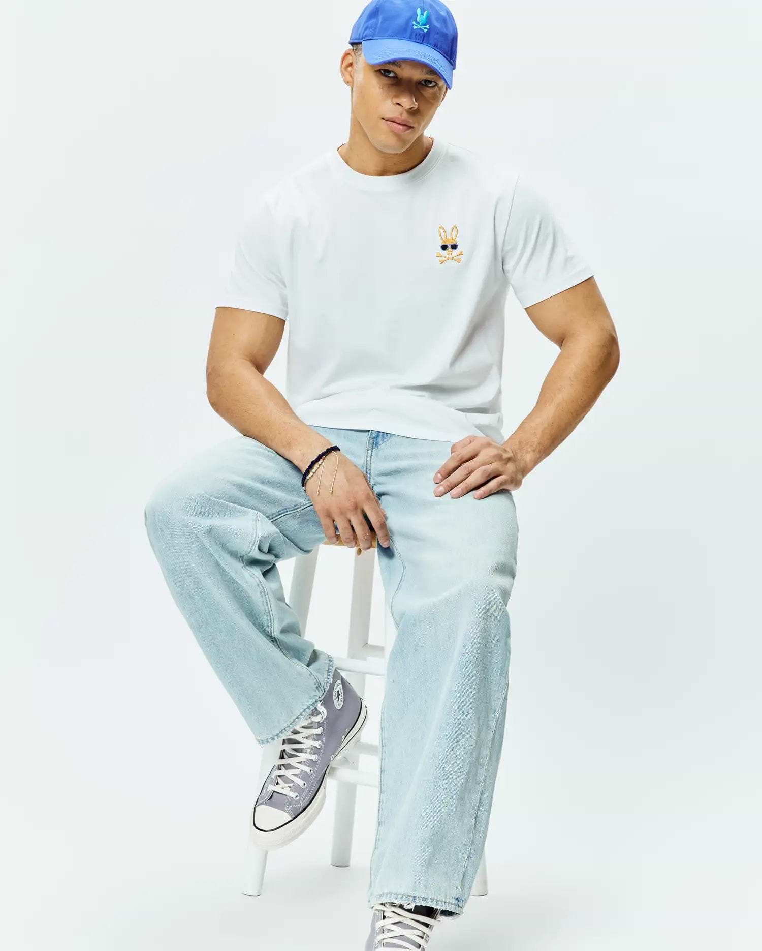 White Mens Sunny Chest Graphic Tee, classic fit, smooth jersey knit, featuring a small embroidered orange and black Psycho Bunny skull with blue sunglasses logo on the left chest.