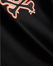 Mens Tanner Bunny Graphic Tee, black jersey knit with a prominent embroidered Psycho Bunny skull logo on the chest, featuring a black skull, white bones, and a vibrant orange outline.