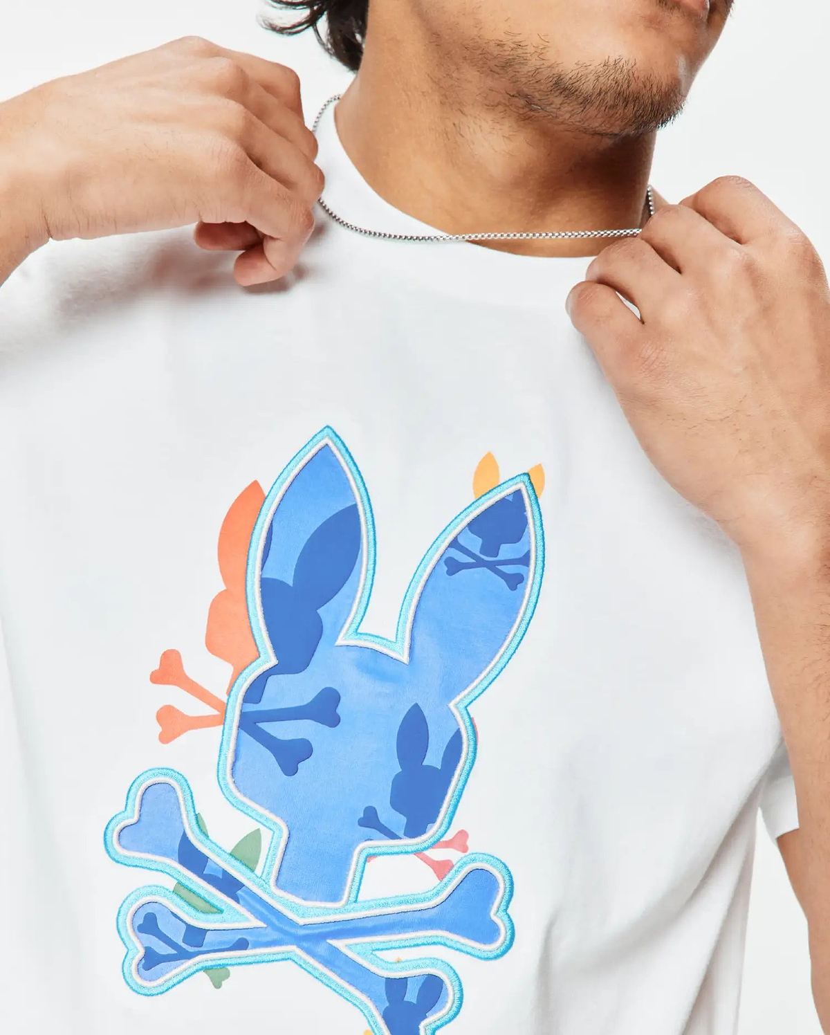Mens Tanner Bunny Graphic Tee, a white classic fit jersey t-shirt featuring a large central blue camouflage bunny skull logo with light blue outline and crossed bones, accented with orange and pink details. (3)