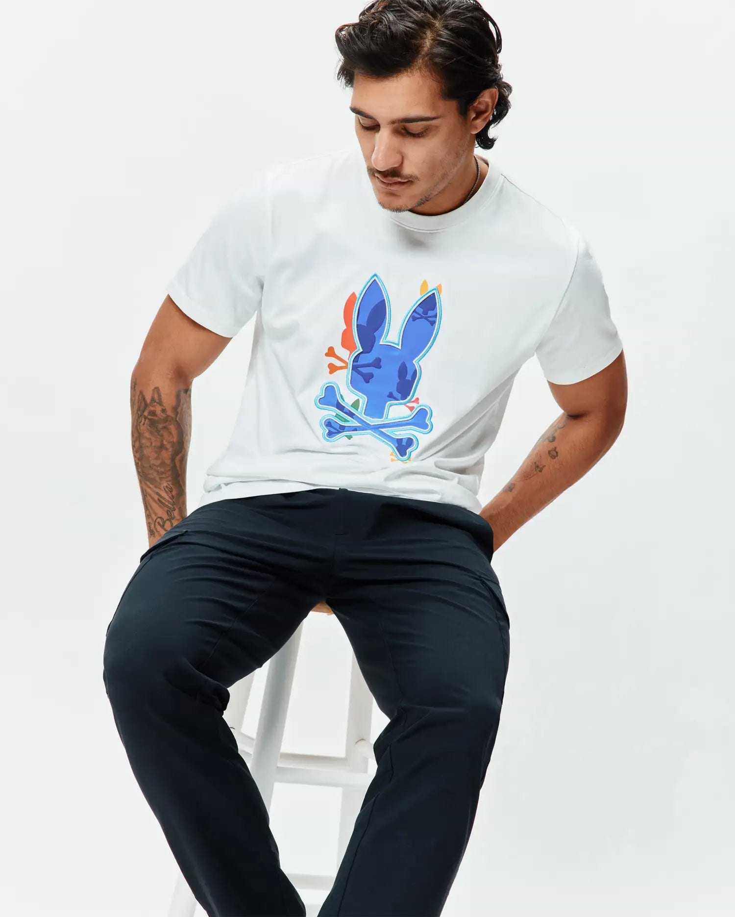 Mens Tanner Bunny Graphic Tee, a classic fit white jersey t-shirt featuring a large central blue Psycho Bunny skull and crossbones graphic with orange and light blue accents. (4)