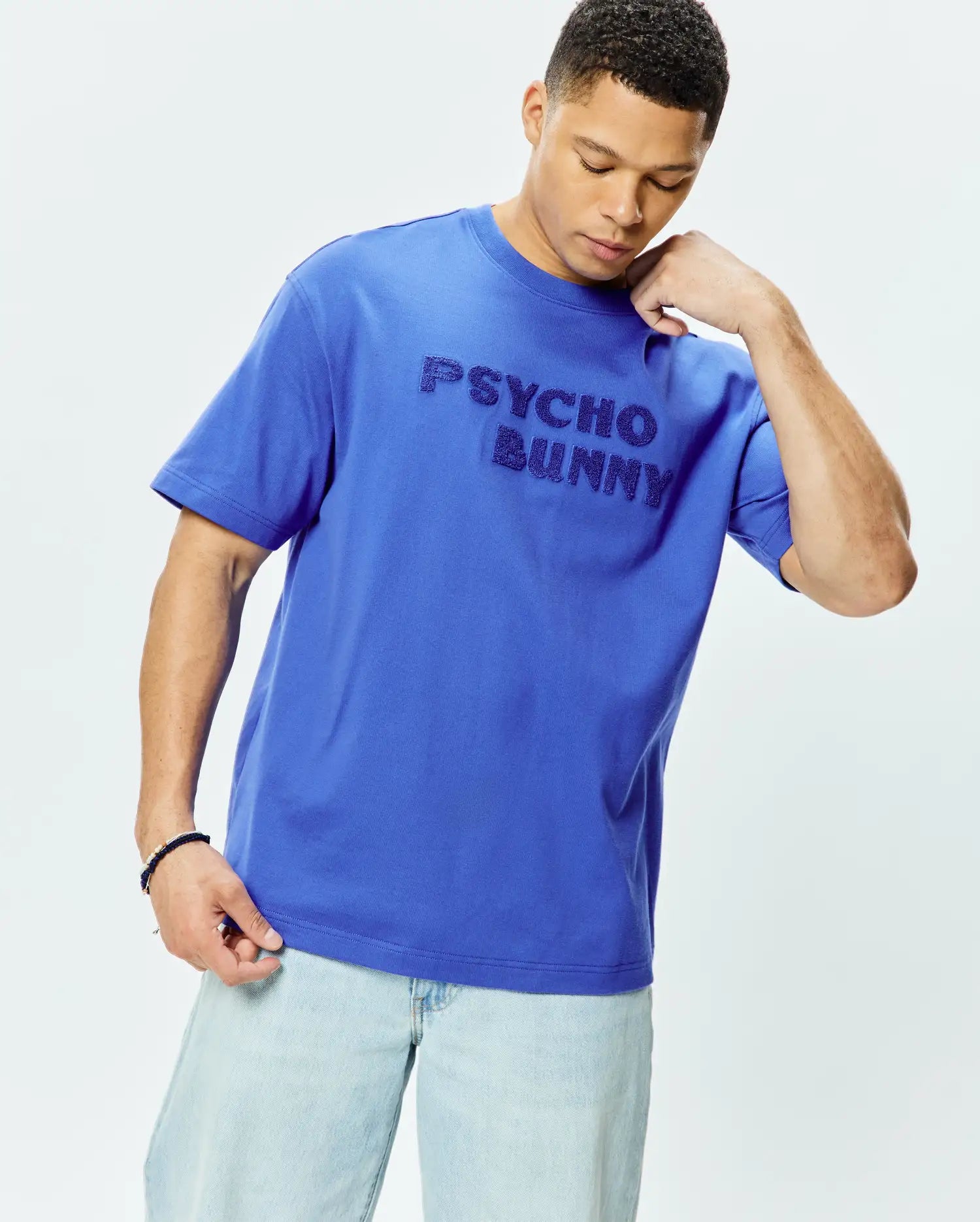 Mens Craig Wordmark Tee, a vibrant royal blue relaxed fit jersey knit t-shirt featuring a prominent, textured tonal Psycho Bunny wordmark across the chest.