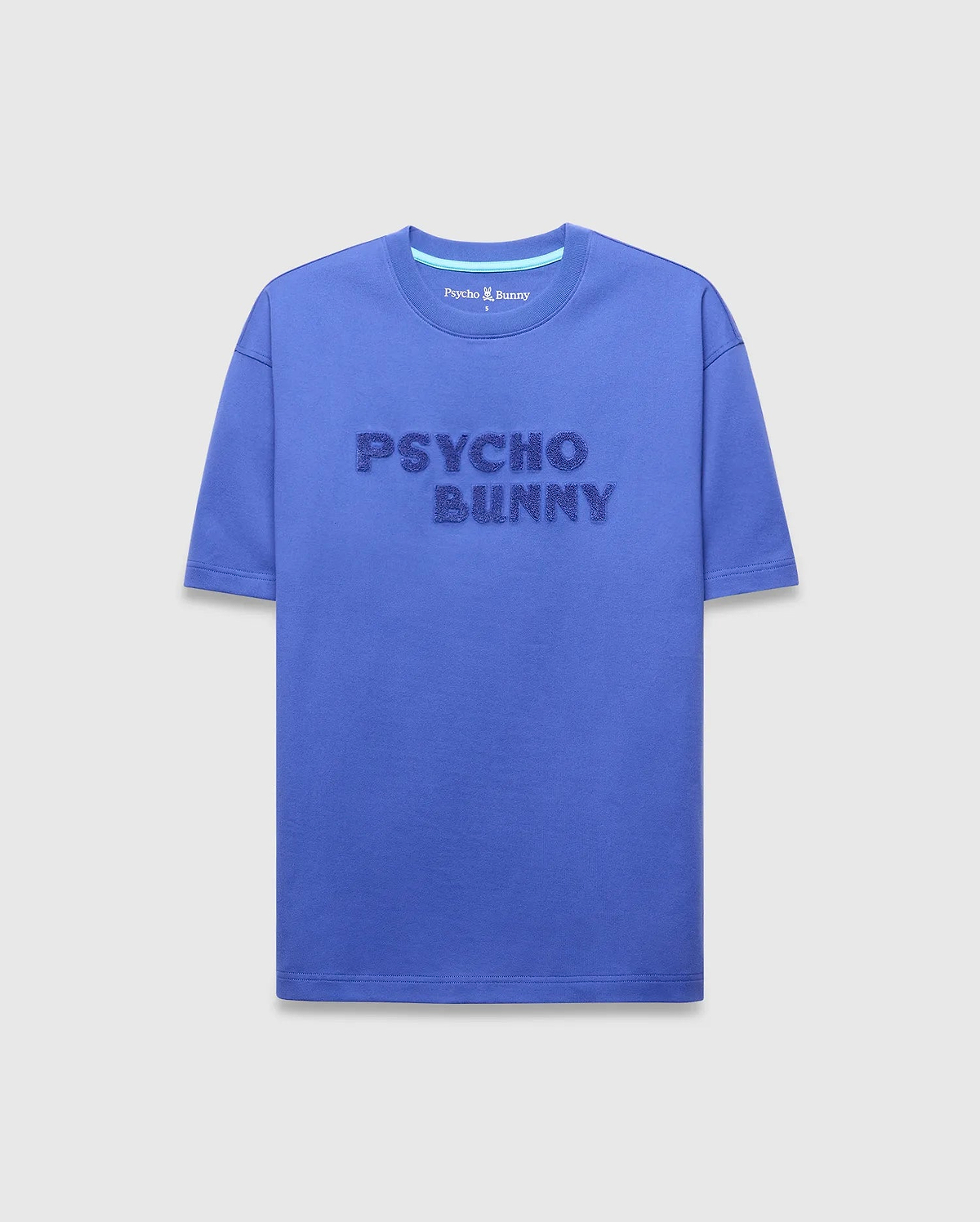 Royal blue Mens Craig Wordmark Tee, a relaxed fit jersey t-shirt featuring a large, textured embossed Psycho Bunny wordmark on the chest and a light blue neck tape.