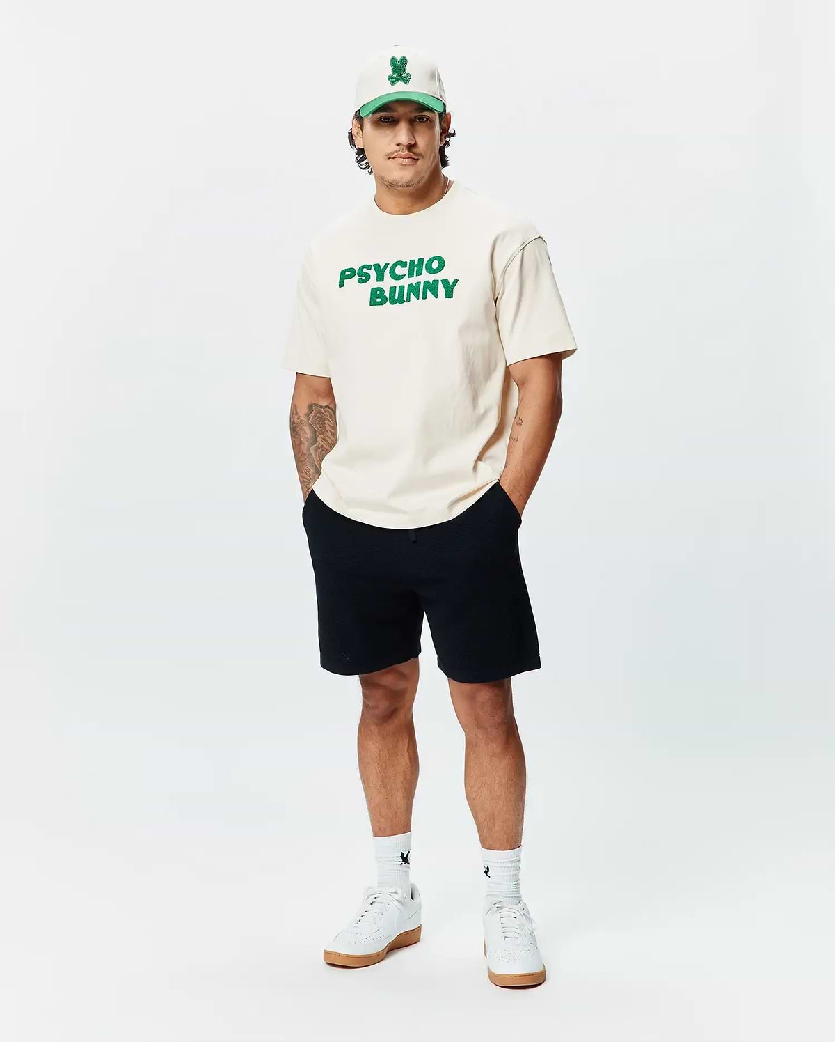 Cream Mens Craig Wordmark Tee, a relaxed fit jersey t-shirt featuring a large, bold green PSYCHO BUNNY wordmark graphic prominently displayed on the chest.